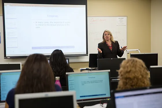 A person presents using a powerpoint presentation to a group of people at computers